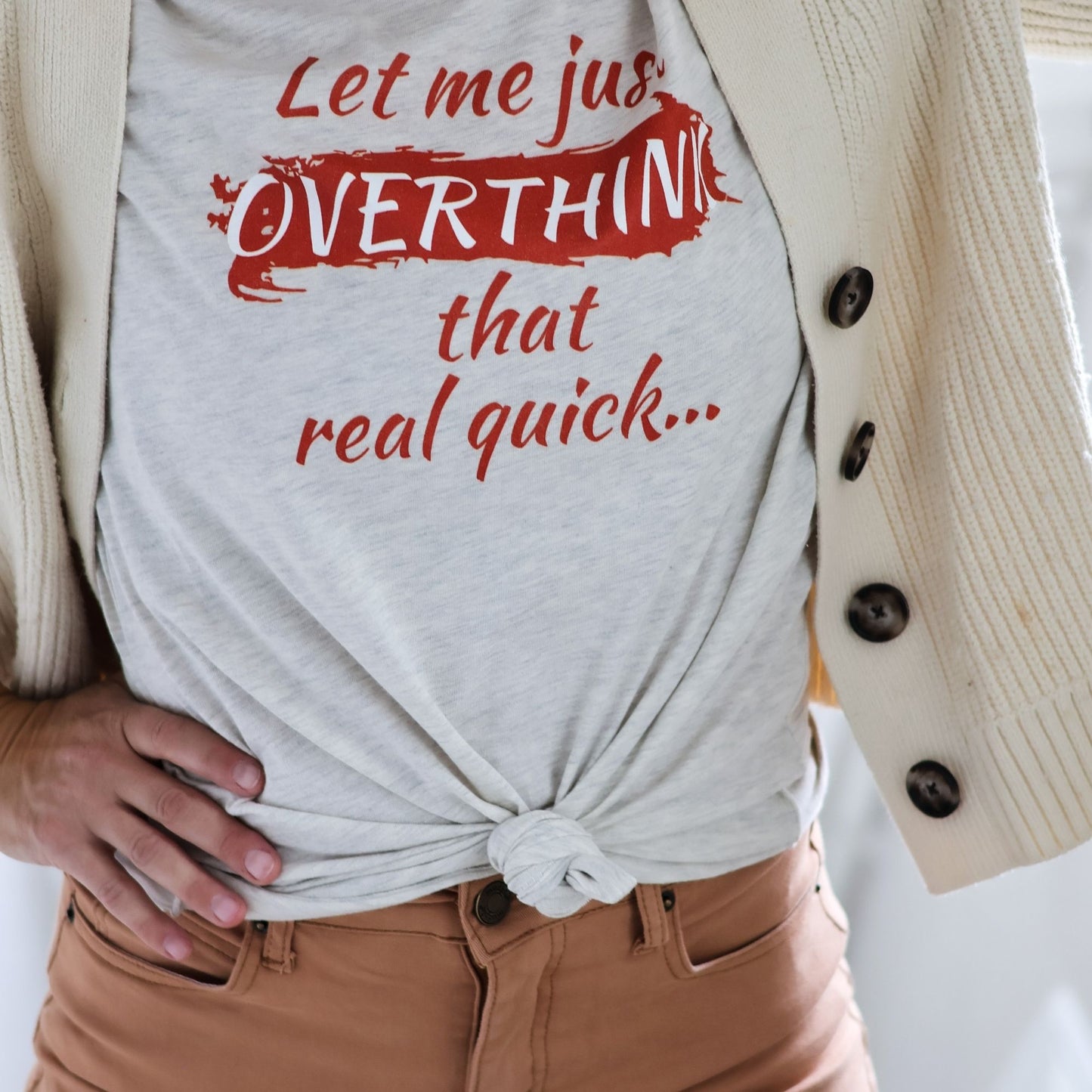Cream colored Let me just overthink that real quick tee with burnt orange text is styles with a front knot, tan pants, and a cardigan.