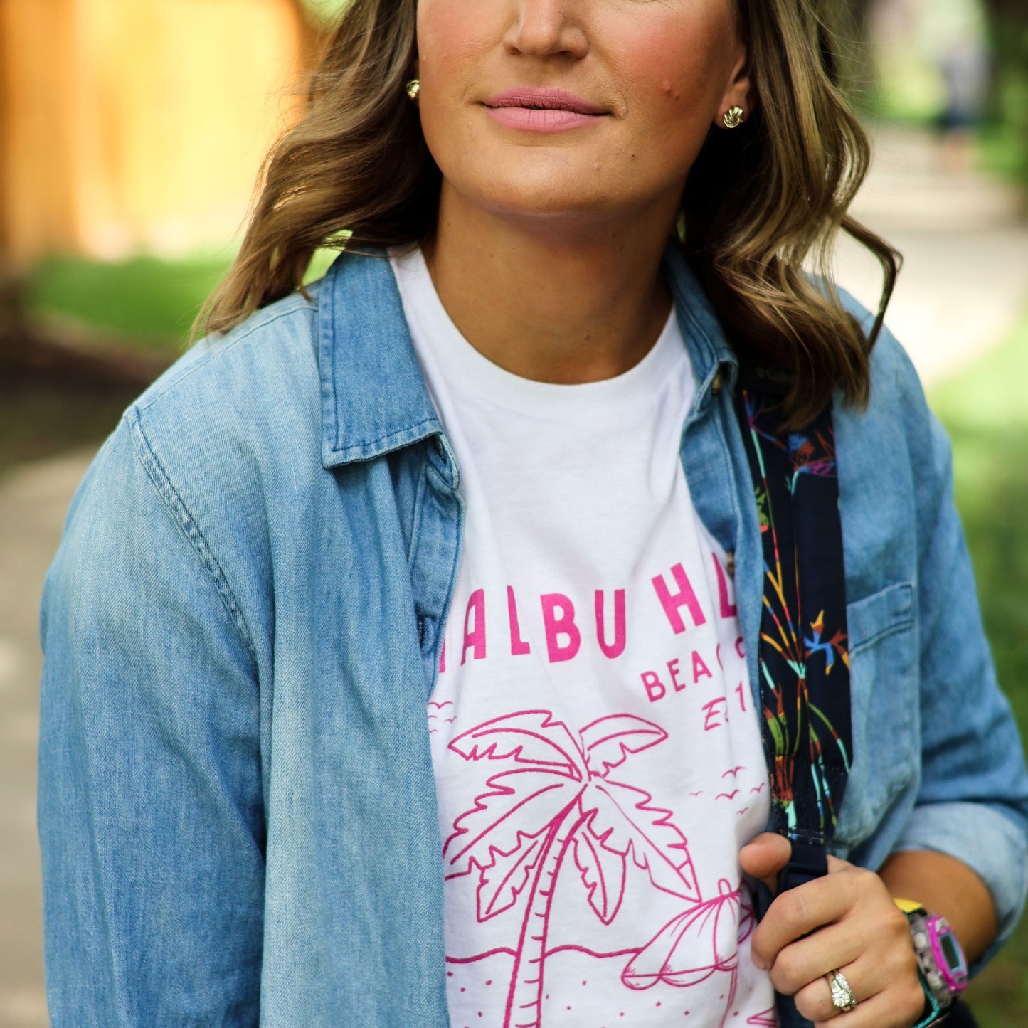 Woman wearing a white t-shirt with pink text and graphics, paired with a denim jacket outdoors.