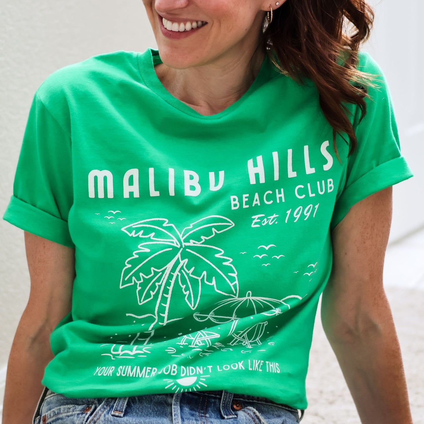 Woman wearing a nostalgic Malibu Hills Beach Club Graphic Tee in kelly green.