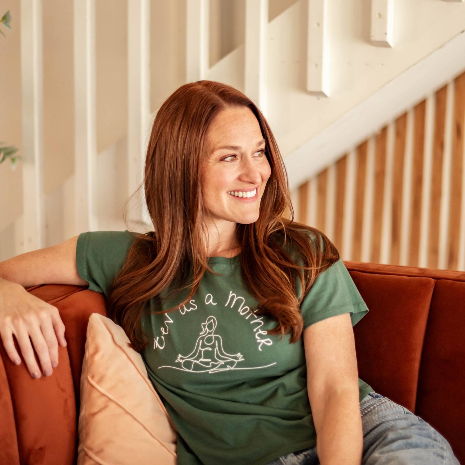 Women wears zen as a mother graphic tee in pine green, smiling on couch