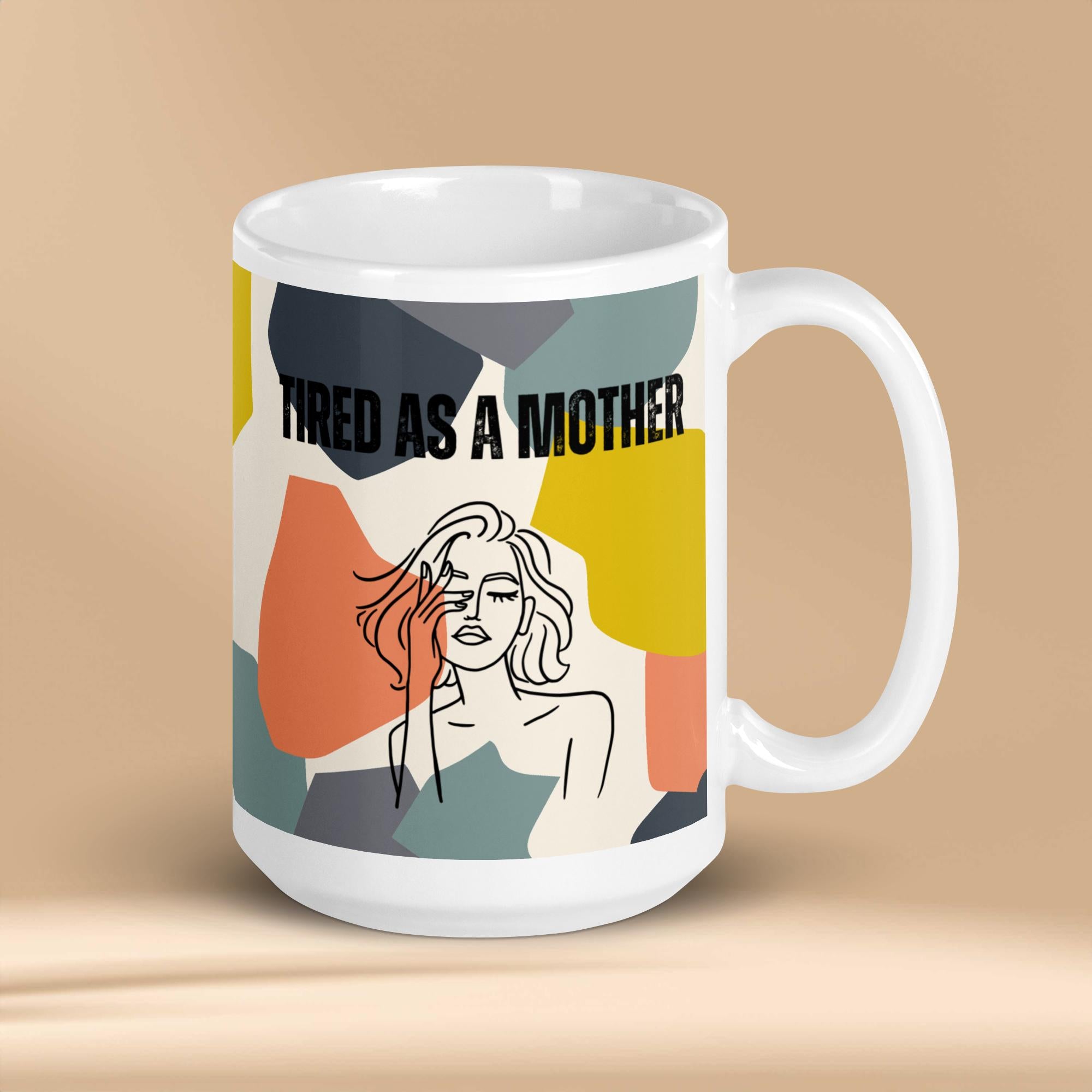 A white ceramic mug featuring the text "TIRED AS A MOTHER" and an abstract illustration of a weary woman with tousled hair. The design incorporates a modern, colorful geometric background with shapes in yellow, orange, gray, and teal.