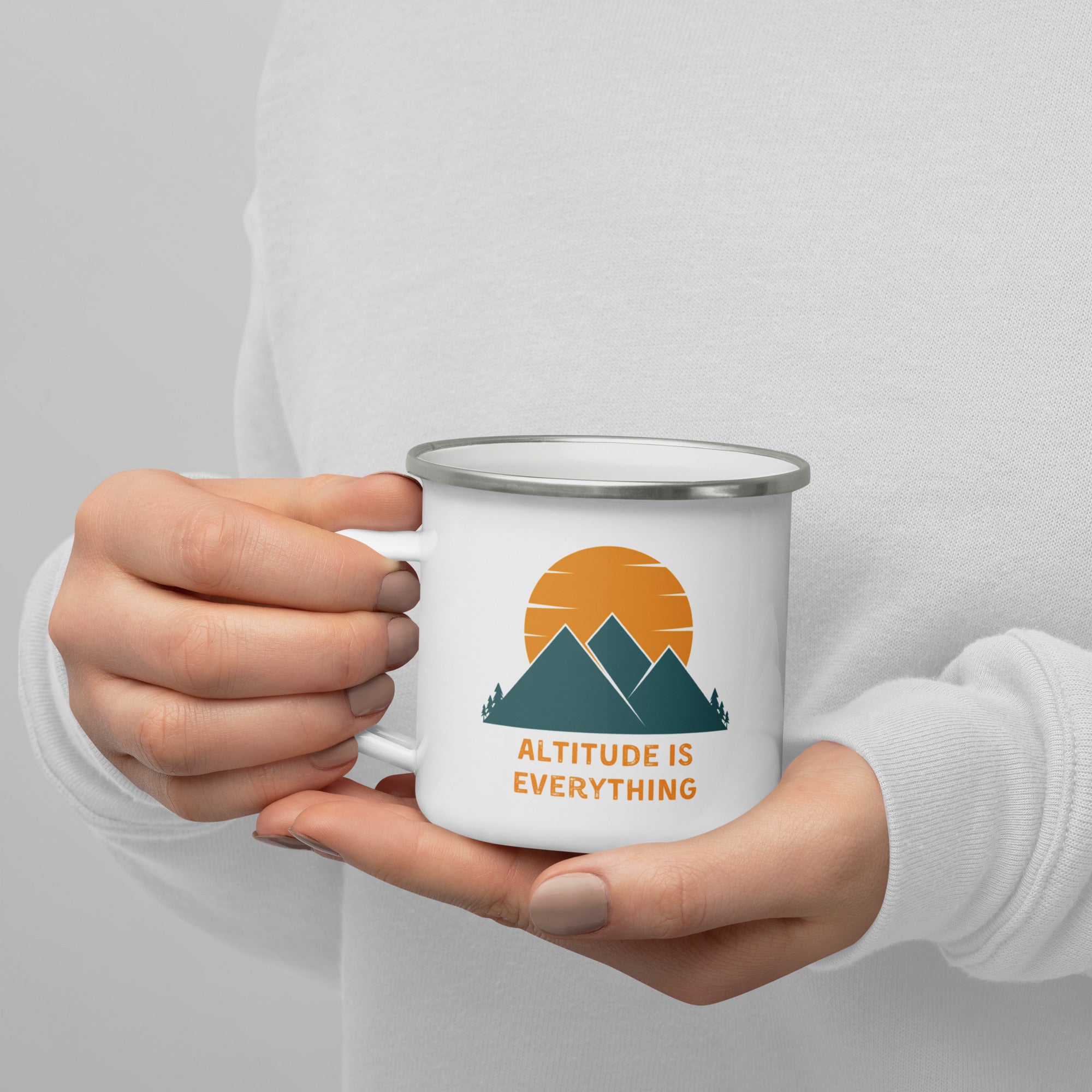 Manicured hands hold a white enamel camping mug that says "altitude is everything" with a mountain and sun graphic.