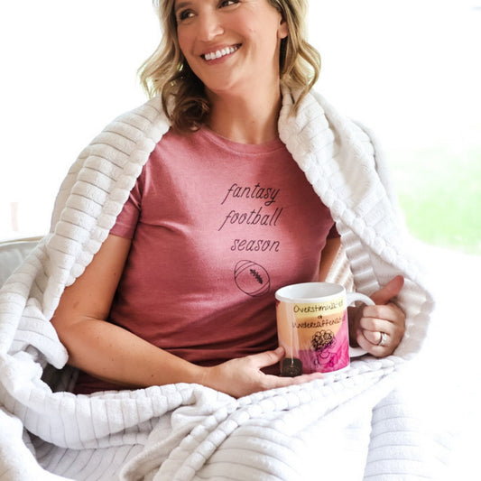 Woman relaxes with a blanket and mug wearing cute fantasy football season womens t-shirt with graphic of football.
