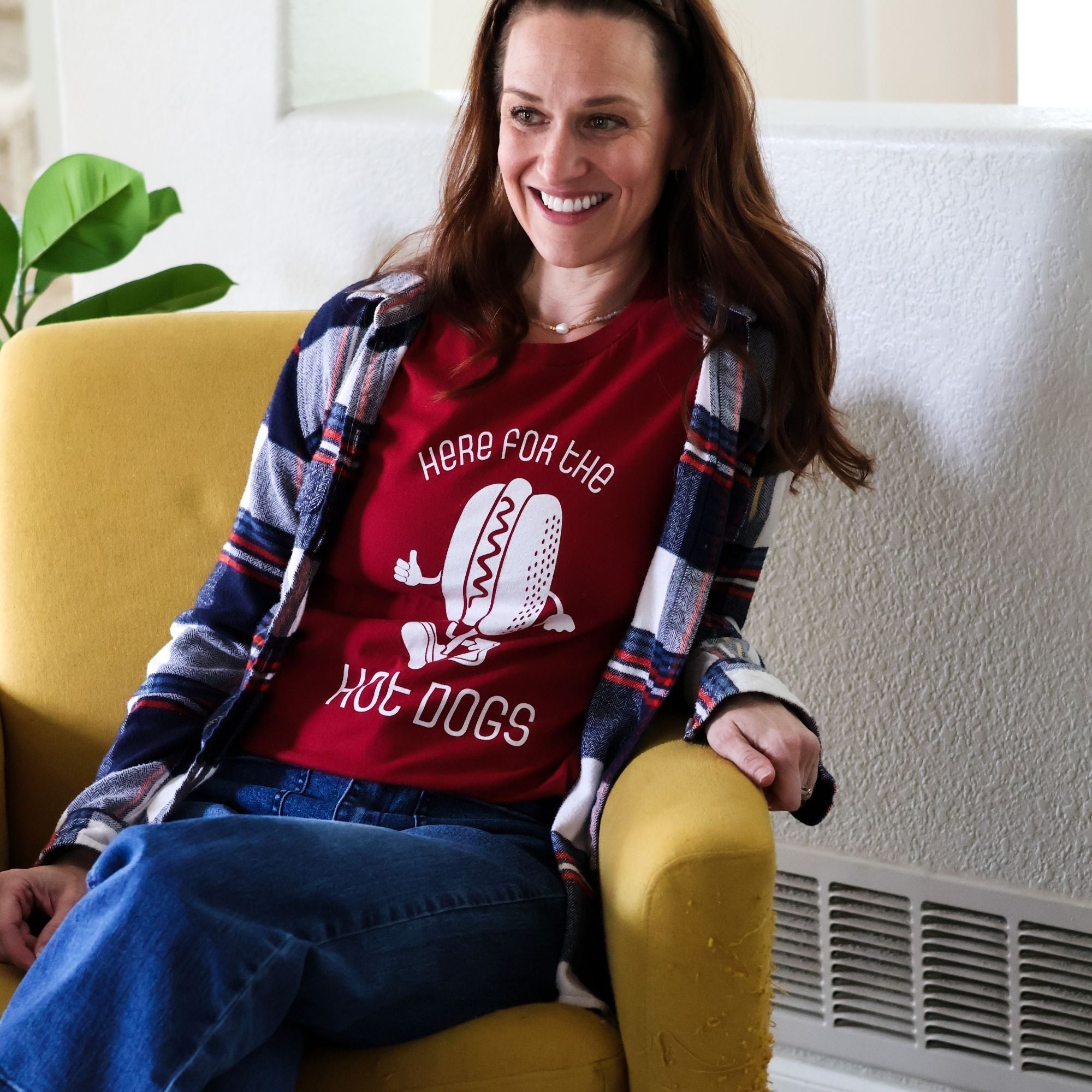Woman socializes while wearing a Here for The Hot Doge Tshirt, plaid flannel shirt, and jeans.