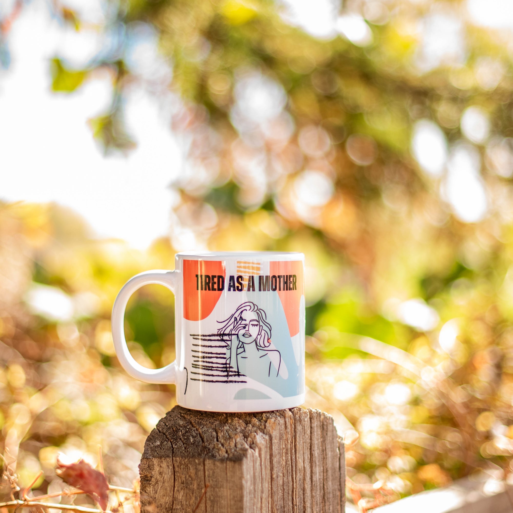 Colorful Tired as a mother mug its on a fence outside