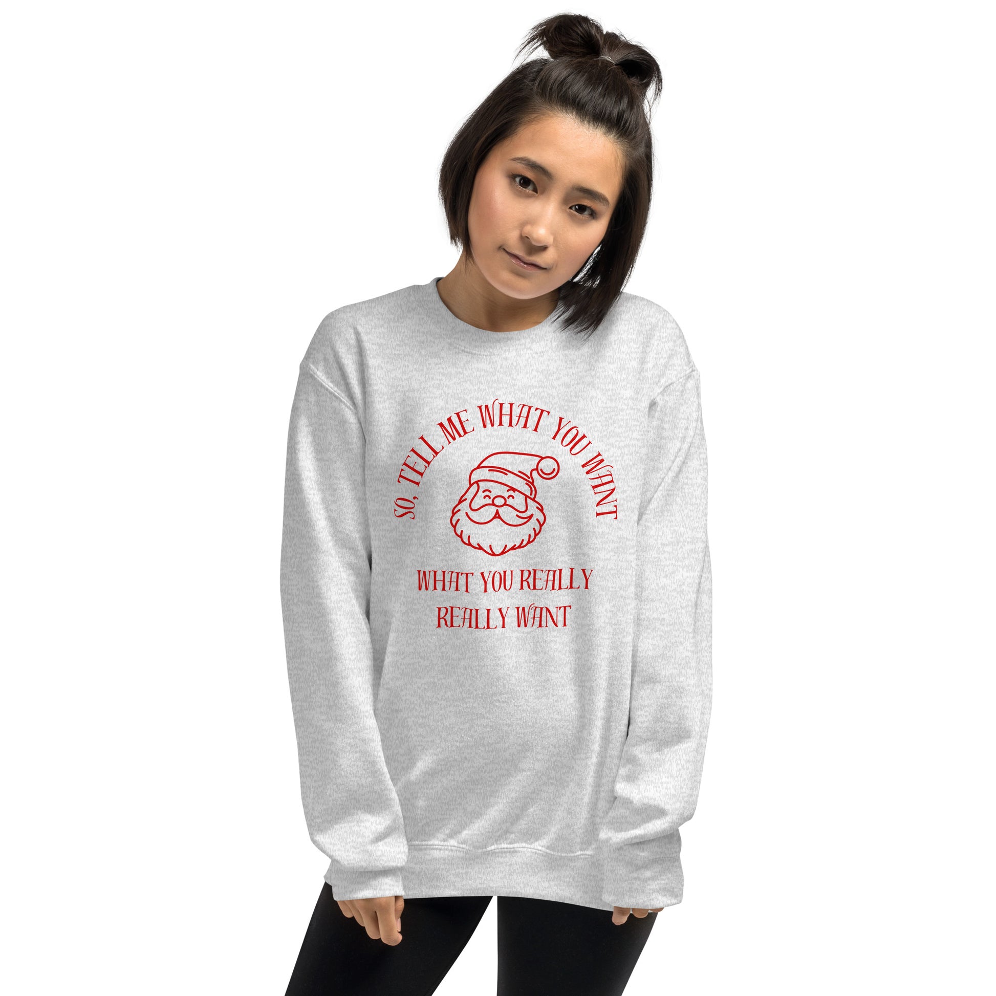 Woman wears a festive crewneck sweatshirt featuring Santa's face and text that reads "So Tell Me What You Want What You Really Really Want," playfully referencing the Spice Girls song while incorporating holiday humor.