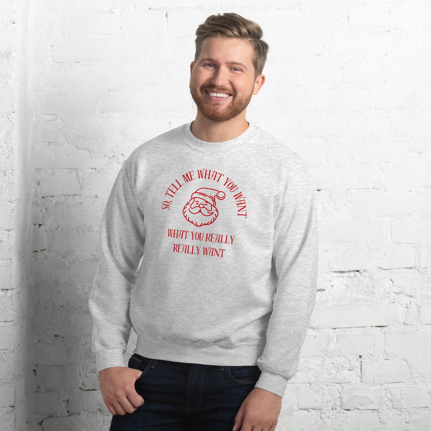 Man wears a festive crewneck sweatshirt featuring Santa's face and text that reads "So Tell Me What You Want What You Really Really Want," playfully referencing the Spice Girls song while incorporating holiday humor.