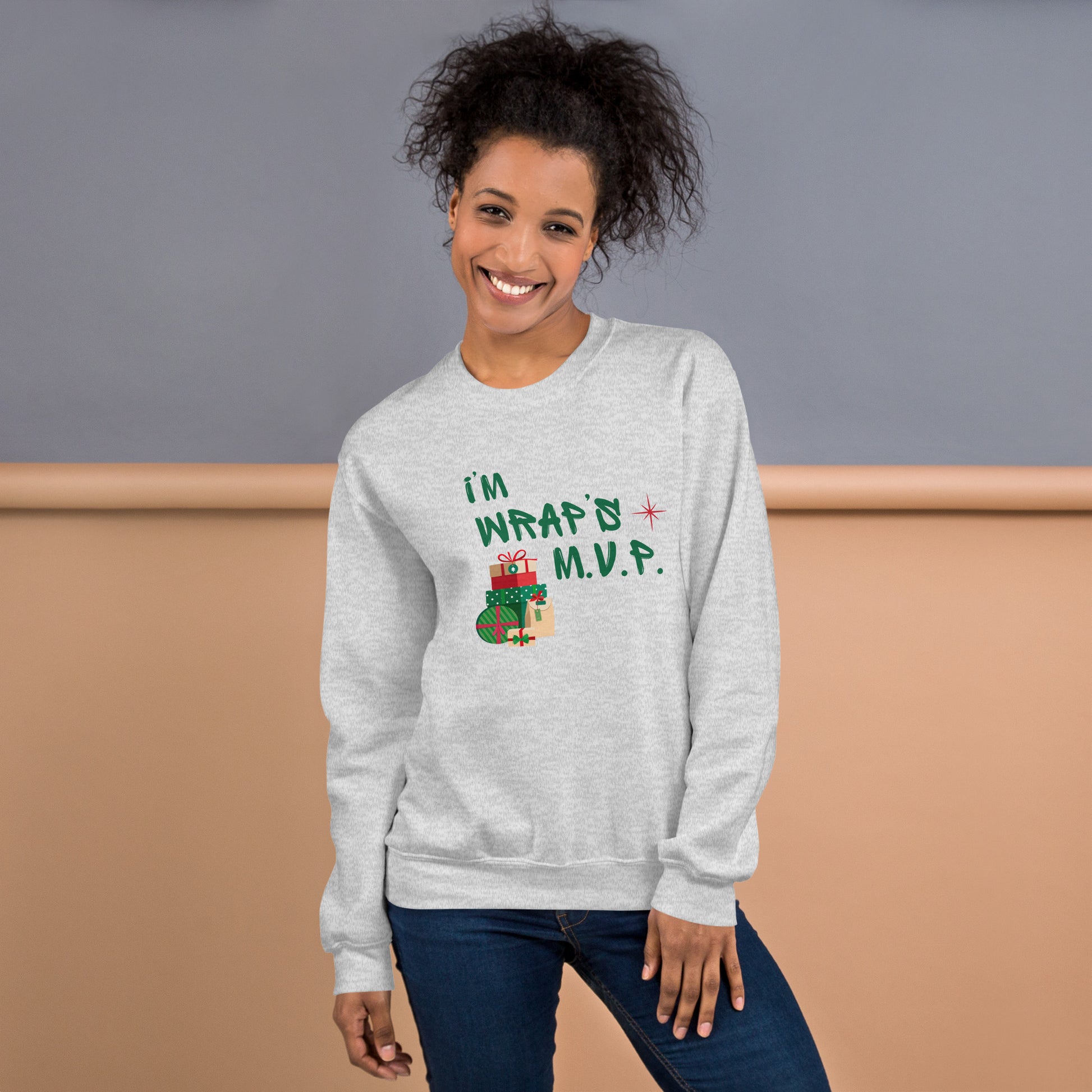 Woman wears cozy gray crewneck sweatshirt with green  text reading 'I'M WRAPs M.V.P.' and festive gift icons. A humorous Christmas play on words for holiday gift-wrapping enthusiasts.