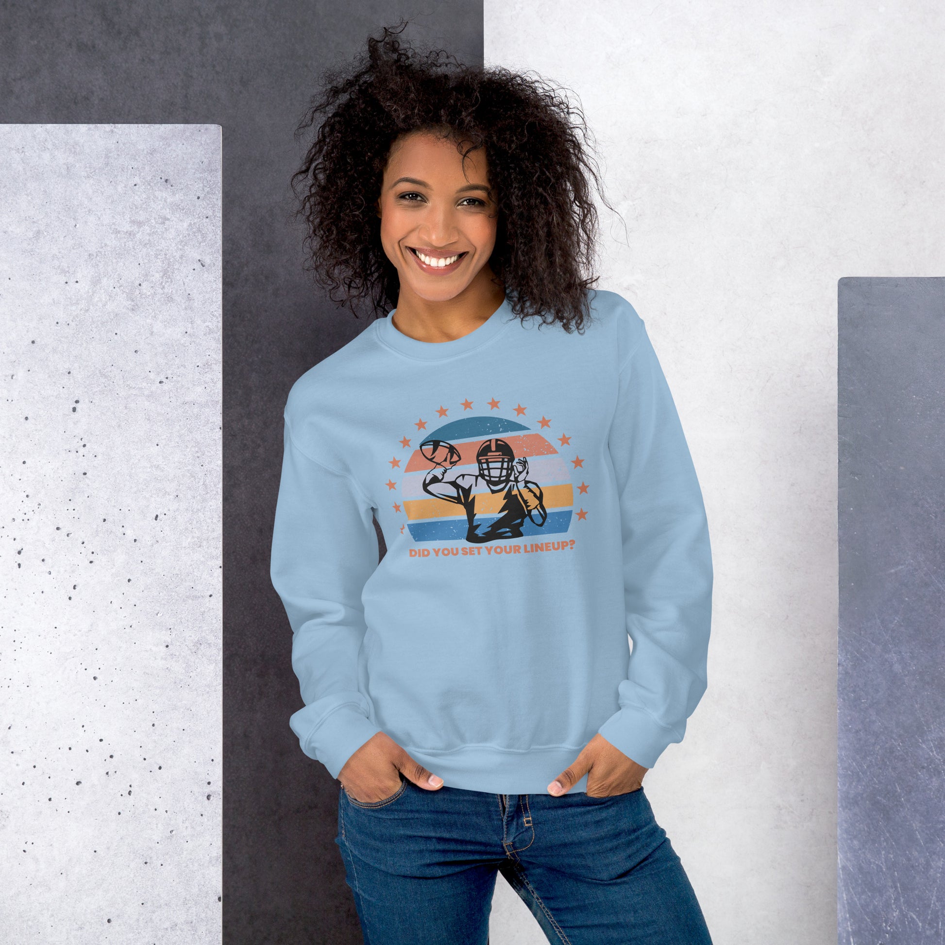 Young woman with curly hair wears a fantasy football sweatshirt that reads "Did you set your line up?" The sweatshirt has a silhouette of a quarterback about the throw a football with a distressed backdrop of yellow, blues, and light pink and a star border.