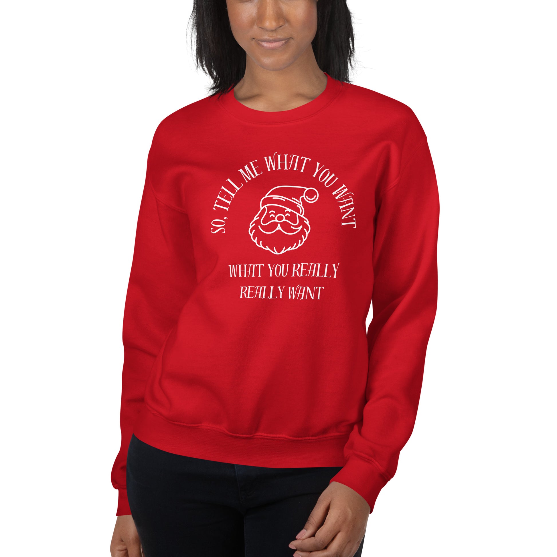 Woman wears a red crewneck sweatshirt featuring Santa's face and text that reads "So Tell Me What You Want What You Really Really Want," playfully referencing the Spice Girls song while incorporating holiday humor.