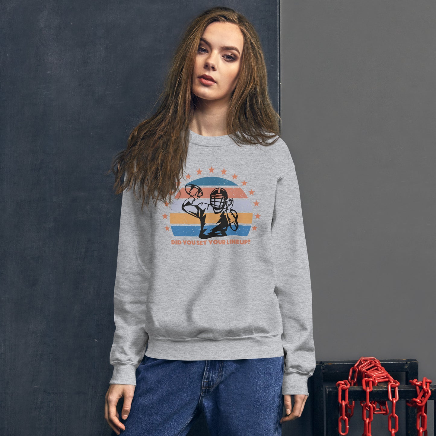 Young woman with long brown hair wears a fantasy football sweatshirt that reads "Did you set your line up?" The sweatshirt has a silhouette of a quarterback about the throw a football with a distressed backdrop of yellow, blues, and light pink and a star border.