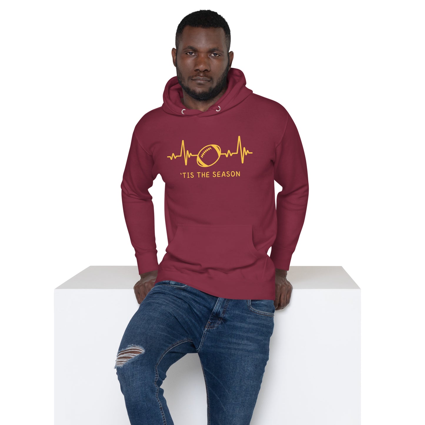 Bearded man wears jeans and a burgundy and gold football sweatshirt - looking like colors for the Washington commanders football team. The burgandy hootdie displays a gold heart rate monitor line with a football in the center. Text reads 'Tis the season" underneath.