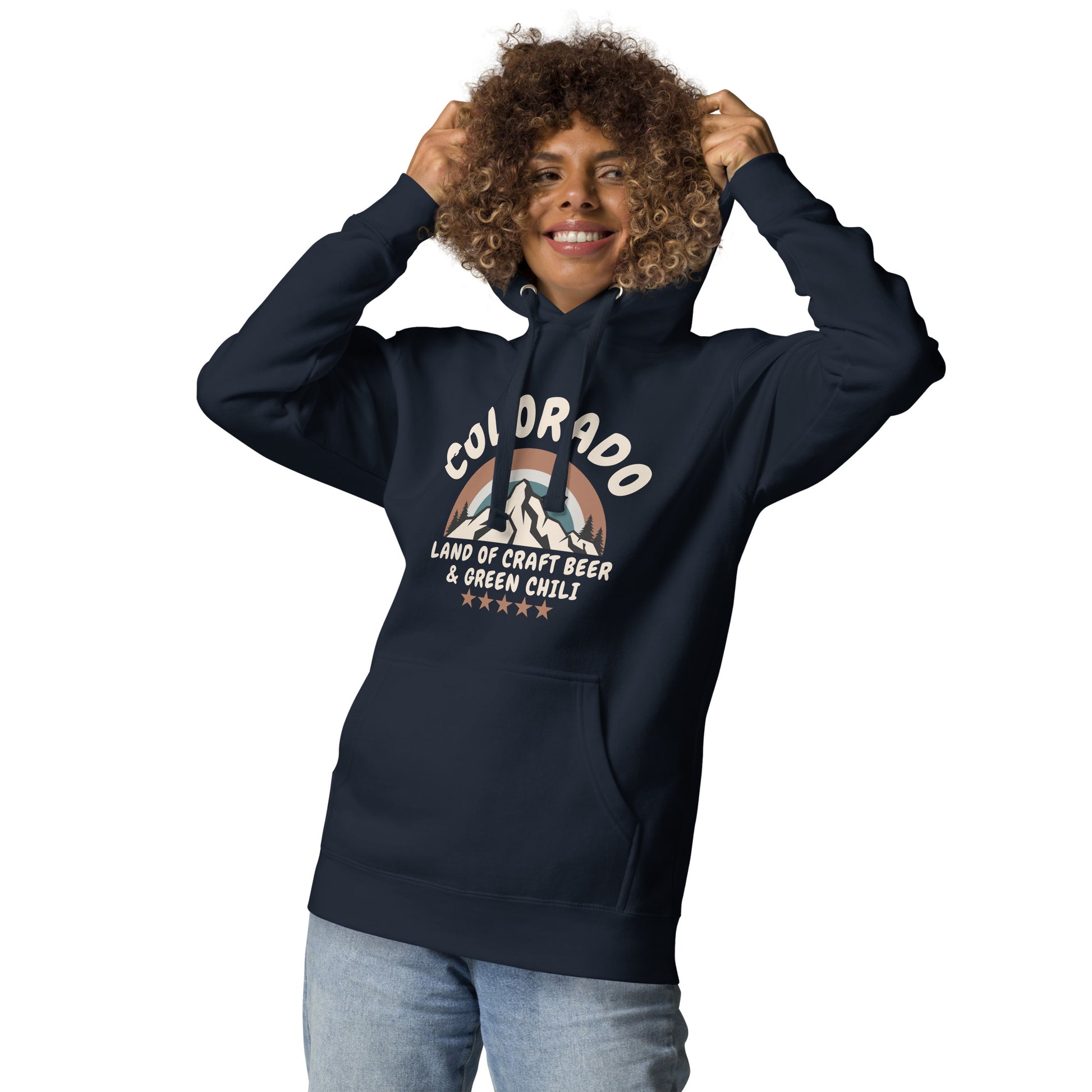 A woman with curly hair smiles while pulling the hood of her navy blue sweatshirt over her head.  The hoodie features text about Colorado with a mountain design and references craft beer and green chili.