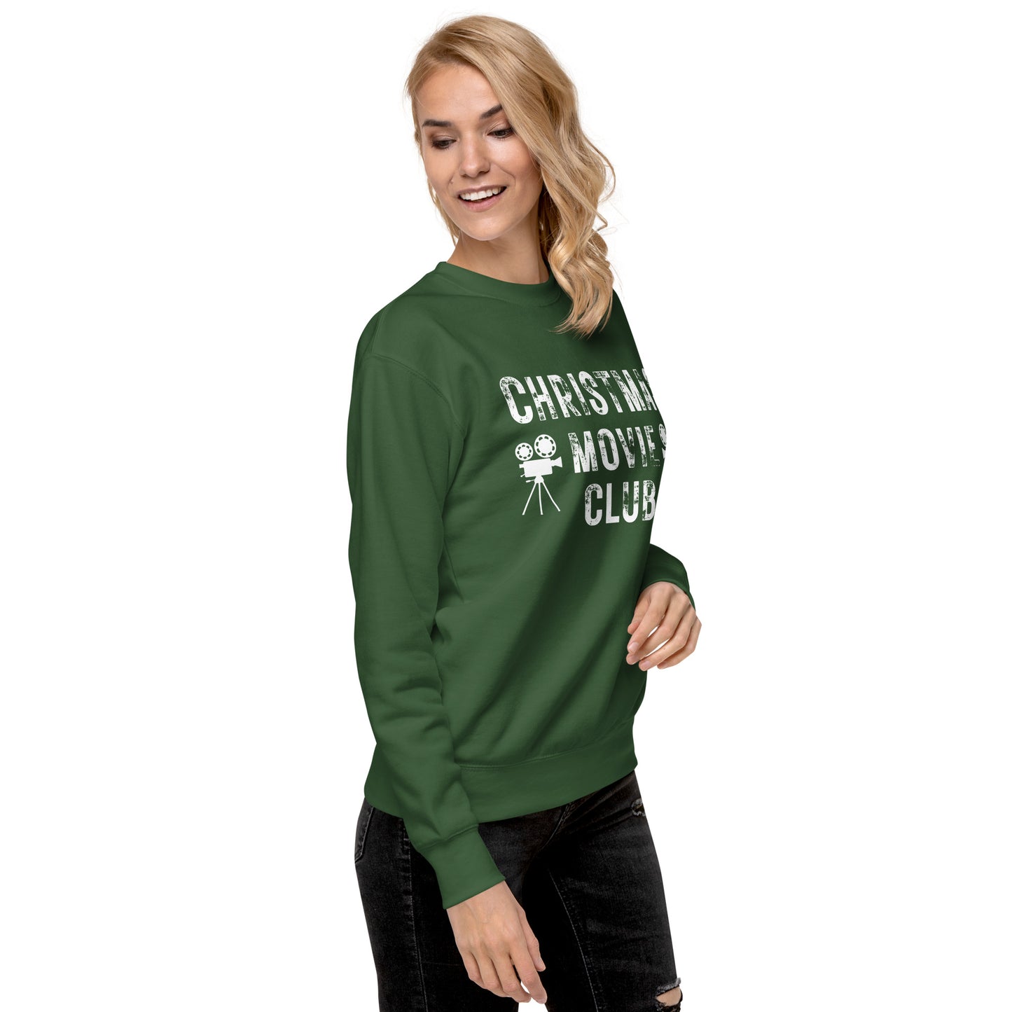 Woman models forest green crewneck sweatshirt with distressed white text reading 'CHRISTMAS MOVIE CLUB', decorated with retro movie camera icons. Perfect for holiday movie marathons.