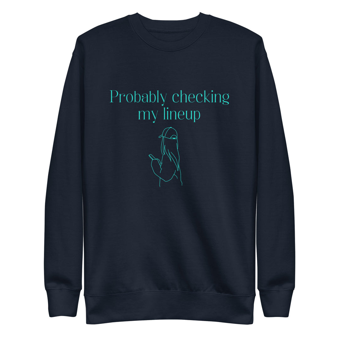 Navy crewneck sweatshirt with aqua line art and text shows a woman in a baseball cap checking her phone. The shirt reads "PROBABLY CHECKING MY LINEUP", a nod to women fantasy football managers.