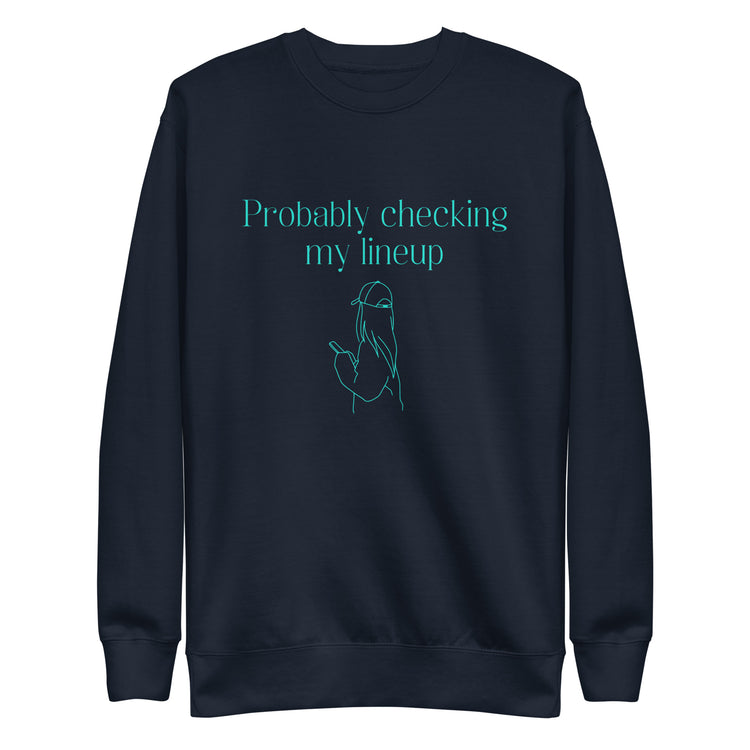 Navy crewneck sweatshirt with aqua line art and text shows a woman in a baseball cap checking her phone. The shirt reads "PROBABLY CHECKING MY LINEUP", a nod to women fantasy football managers.