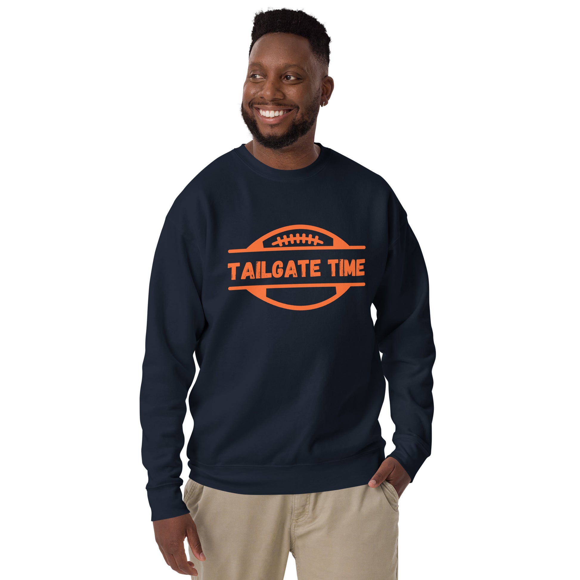 Smiling man wears a navy football sweatshirt with orange graphic and font. The blue crewneck displays an orange football graphic with the word "tailgate time" in a distressed font. The colors are perfect for Chicago Bears, Denver Broncos, or university of Illinois fans.