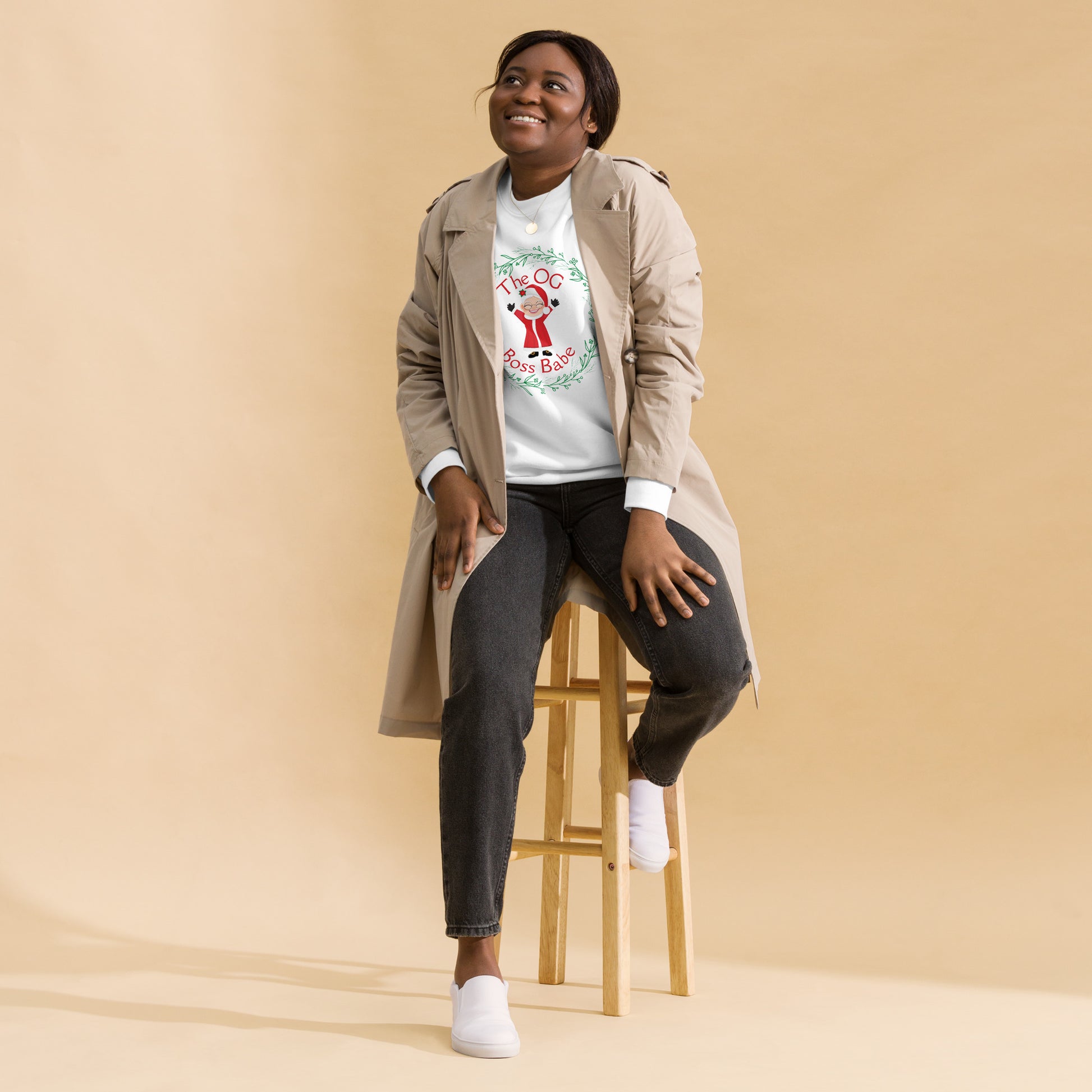 Smiling woman wears a festive crewneck sweatshirt with an image of Mrs. Claus that reads "The OG Boss Babe"