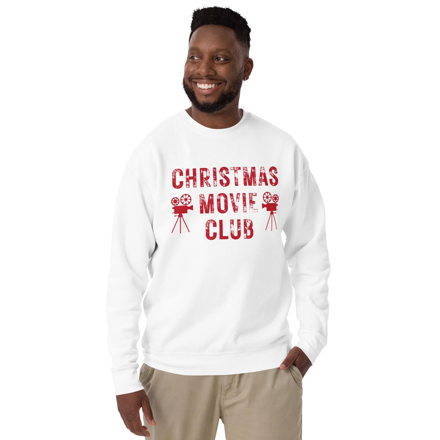 Smiling man models white crewneck sweatshirt with distressed red text reading 'CHRISTMAS MOVIE CLUB', decorated with retro movie camera icons. Perfect for holiday movie marathons.