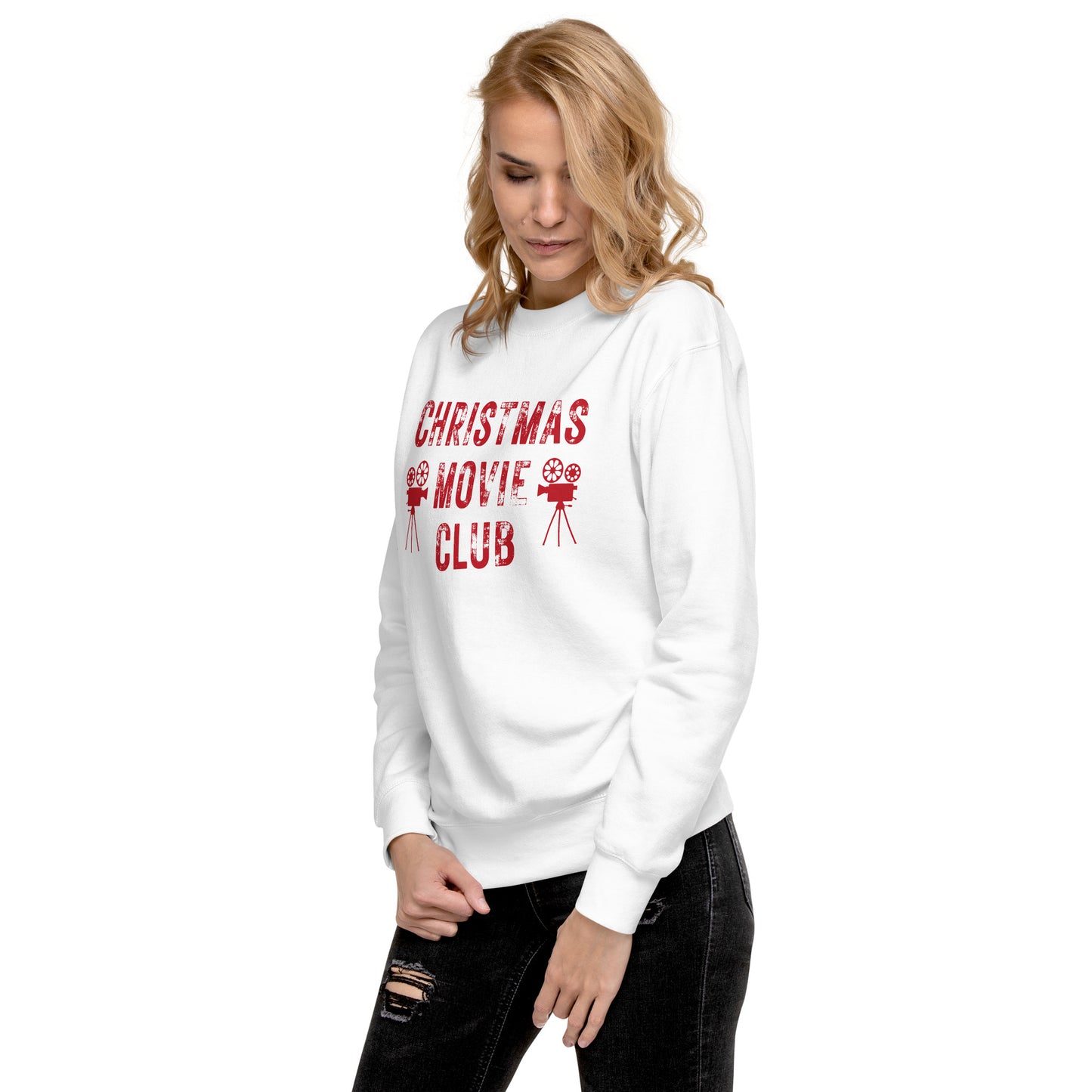 Woman models white crewneck sweatshirt with distressed red text reading 'CHRISTMAS MOVIE CLUB', decorated with retro movie camera icons. Perfect for holiday movie marathons.