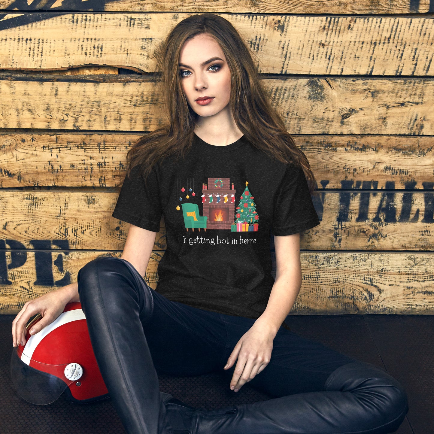 Woman wears holiday tee shirt that reads "It's getting hot in herre". The design is a cozy Christmas living room with holiday decorations and a roaring fireplace.