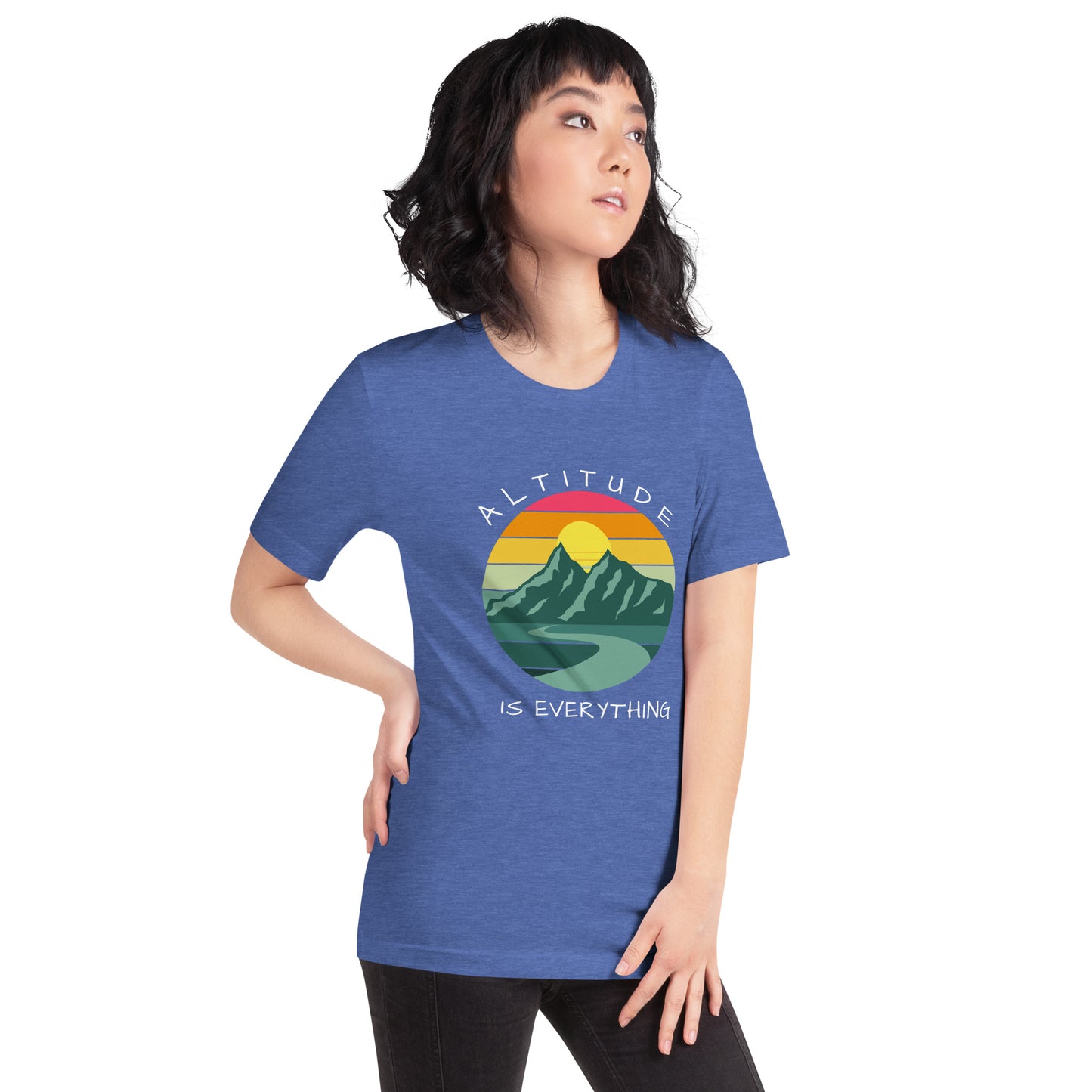 Woman with dark hair wears jeans and a heather blue graphic tee that reads "ALTITUDE IS EVERYTHING." The image is a beautiful mountain scene with a colorful sunset. 