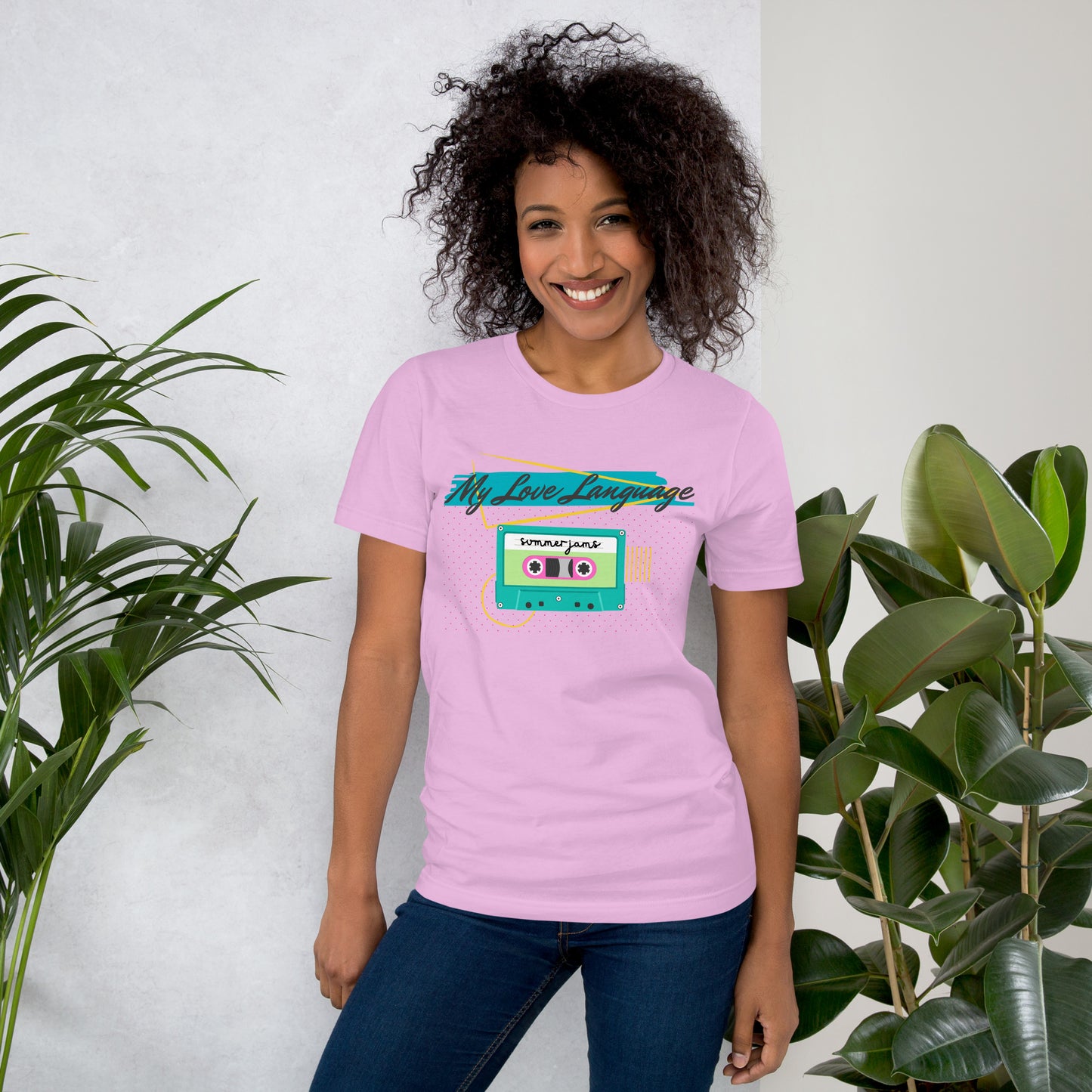 A woman wears a lilac purple tee with bright pink, blue, yellow and green graphics from the 80s and 90s. The shirt reads "MY LOVE LANGUAGE" and features a cassette tape - a reference to the mixtape era.