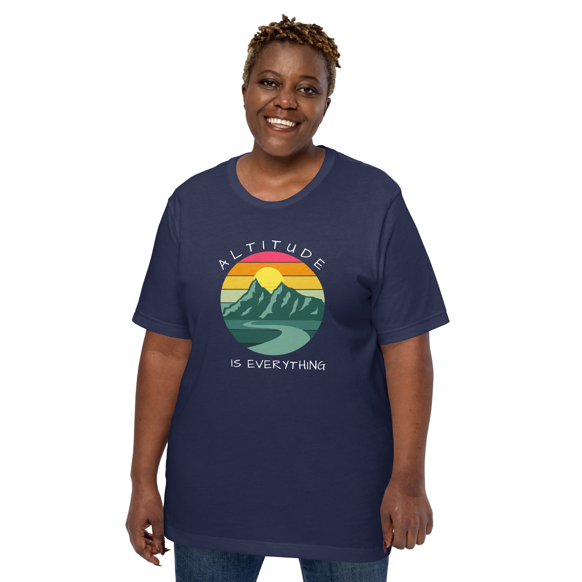 Smiling woman with short hair wears jeans and a navy graphic tee that reads "ALTITUDE IS EVERYTHING." The image is a beautiful mountain scene with a colorful sunset. 