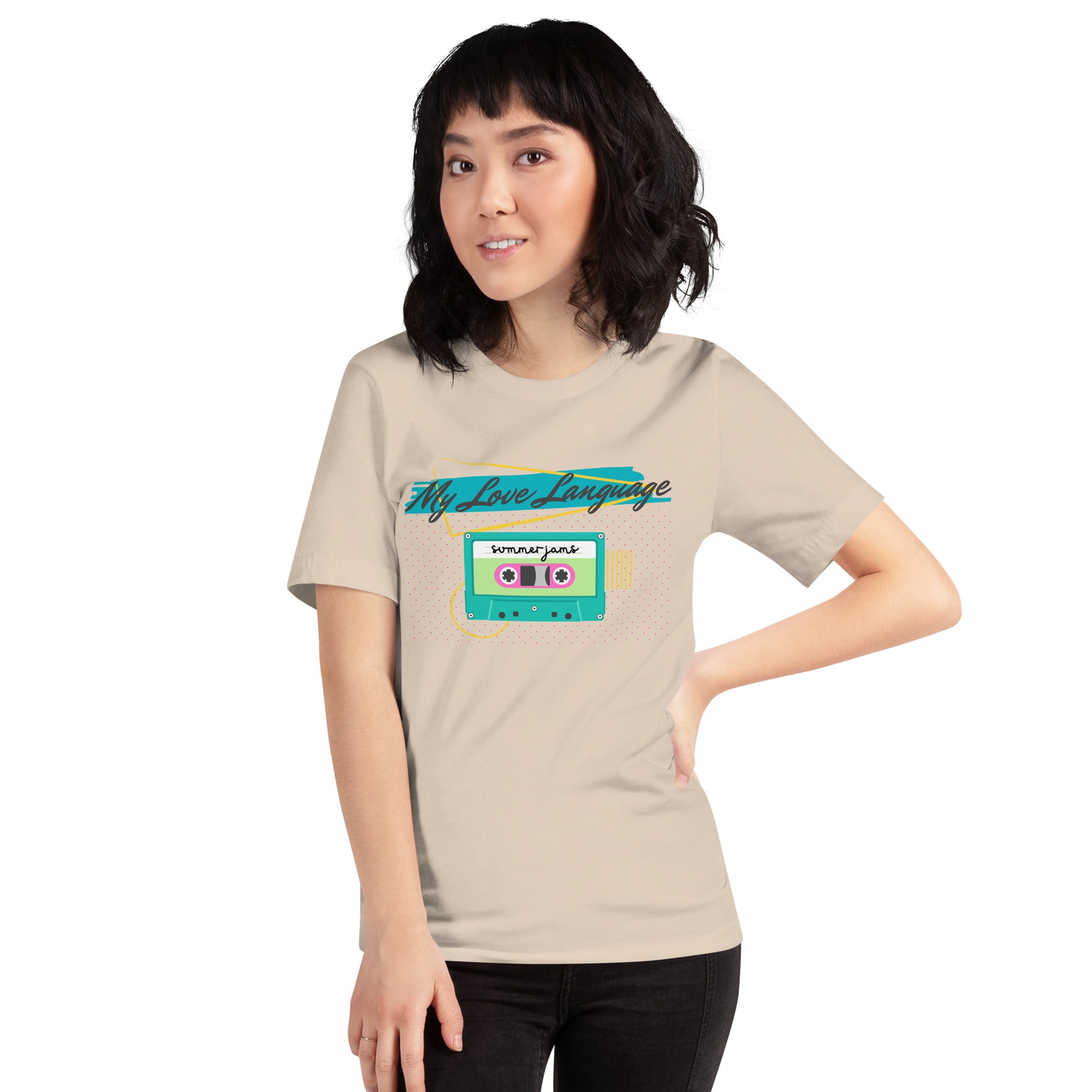 A woman wears a neutral colored tee with bright pink, blue, yellow and green graphics from the 80s and 90s. The shirt reads "MY LOVE LANGUAGE" and features a cassette tape - a reference to the mixtape era.