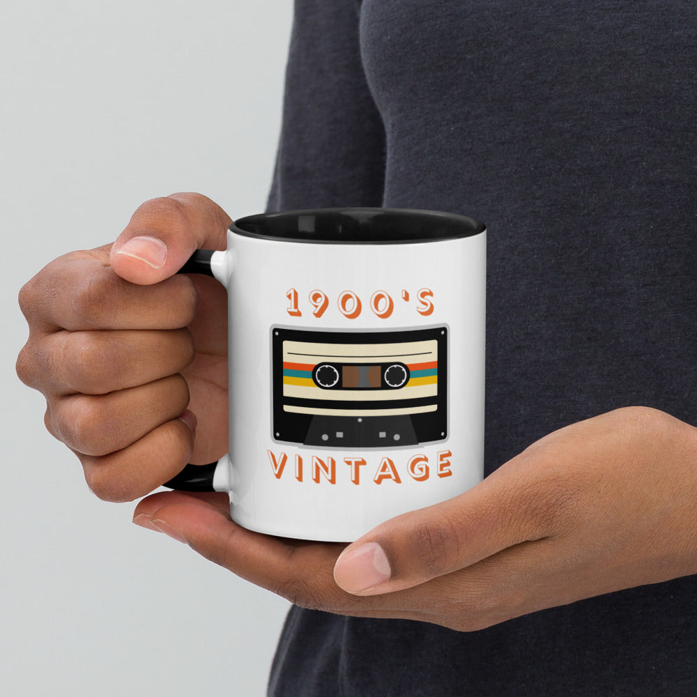 A pair of hands cups a ceramic mug with black interior and a black handle. It displays a retro looking cassette tape and the words "1900s VINTAGE". A Jade Street Market original mug.