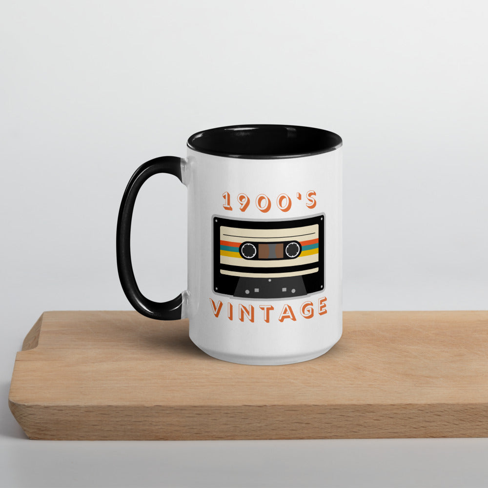 White ceramic mug with black interior and a black handle sits on a wooden surface. It displays a retro looking cassette tape and the words "1900s VINTAGE". A Jade Street Market original mug.