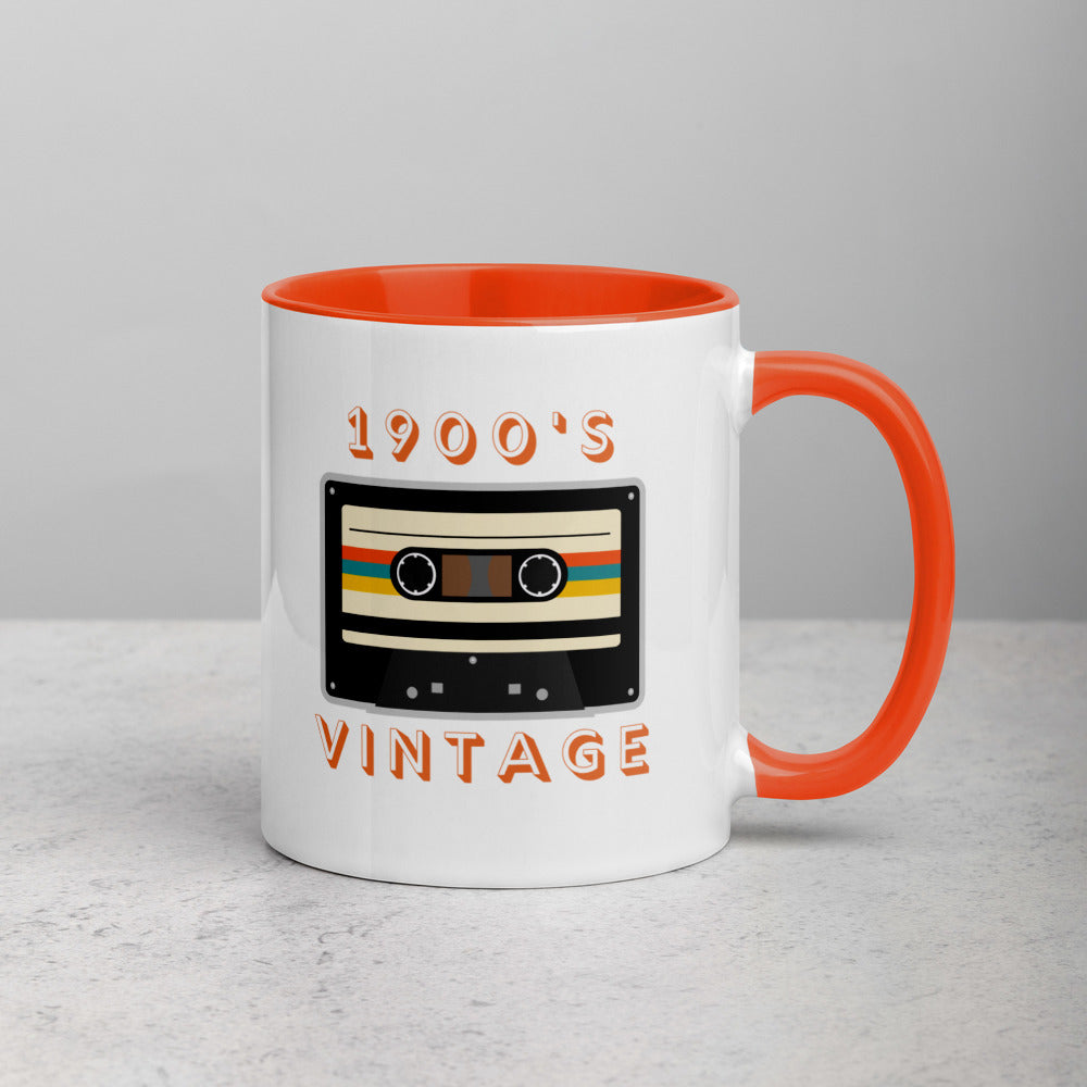 White ceramic mug with orange interior and an orange handle sits on a white surface. It displays a retro looking cassette tape and the words "1900s VINTAGE". A Jade Street Market original mug.