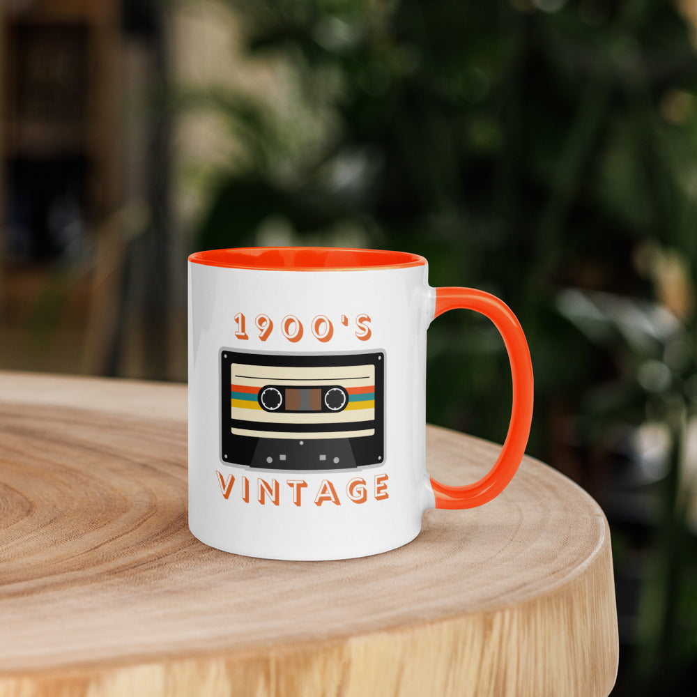 White ceramic mug with orange interior and an orange handle sits on a wooden table. It displays a retro looking cassette tape and the words "1900s VINTAGE". A Jade Street Market original mug.