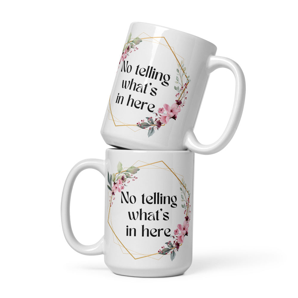 Two white ceramic mugs are stacked on top of each other displaying identical front and back designs -  a floral wreath surrounds the text "No telling what's in here". The mug's design features a delicate floral arrangement in soft pink and green hues, giving it a bohemian, feminine aesthetic.