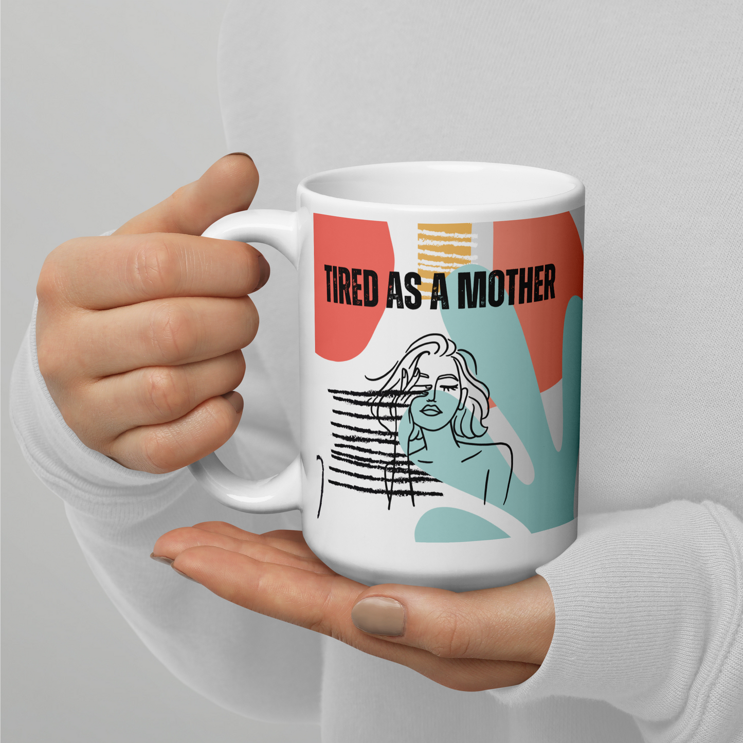 Manicured hands belonging to a person wearing a white sweatshirt cup a colorful coffee mug that reads "TIRED AS A MOTHER". Under the text is line art of a woman with her eyes closed, rubbing one eye. A colorful background pattern includes mint, rosy pink, yellow, coral and black with shapes reminiscent of the 80s or early 90s.