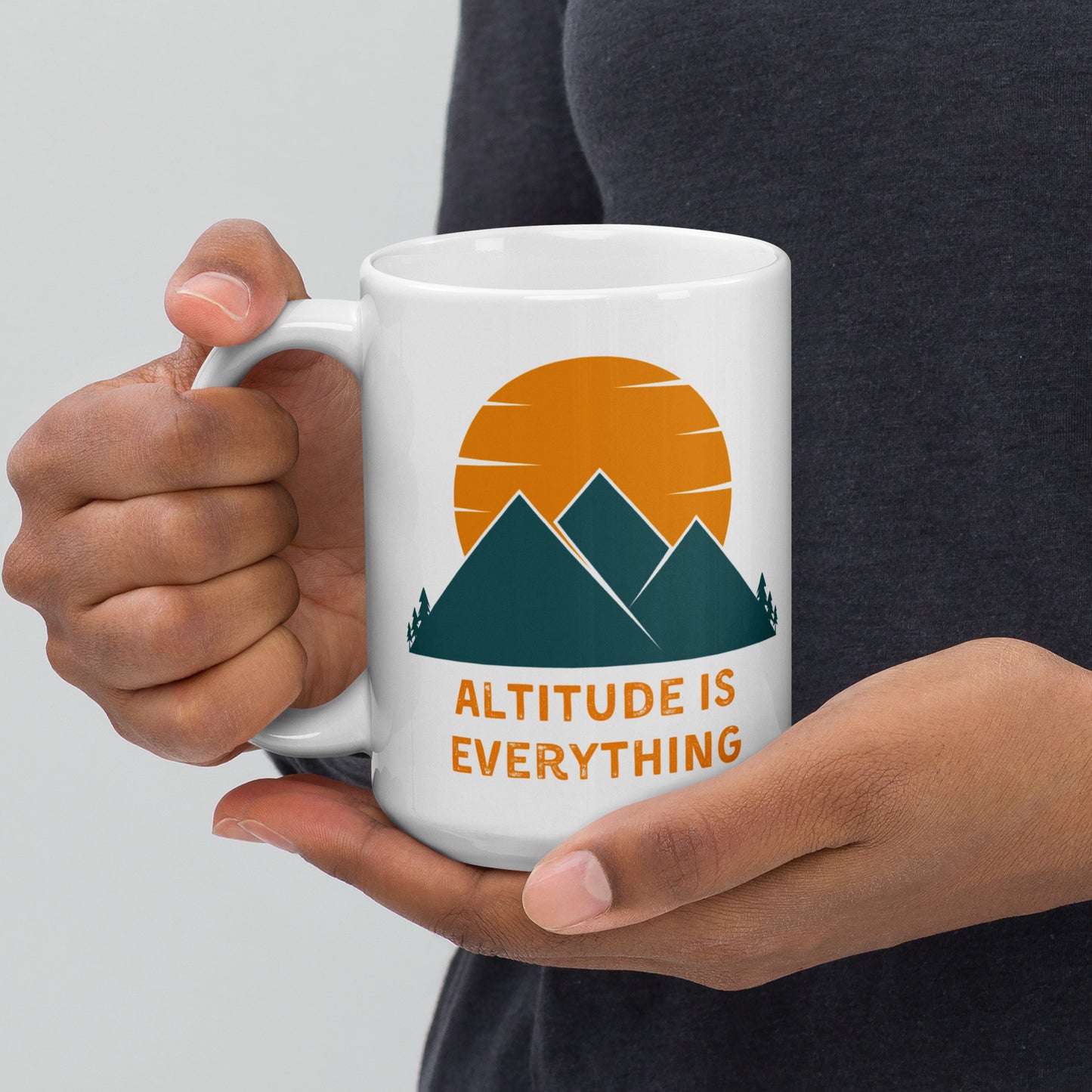 Woman's hands cup a white ceramic mug that says Altitude is Everything with a graphic image of mountains and a sunset.