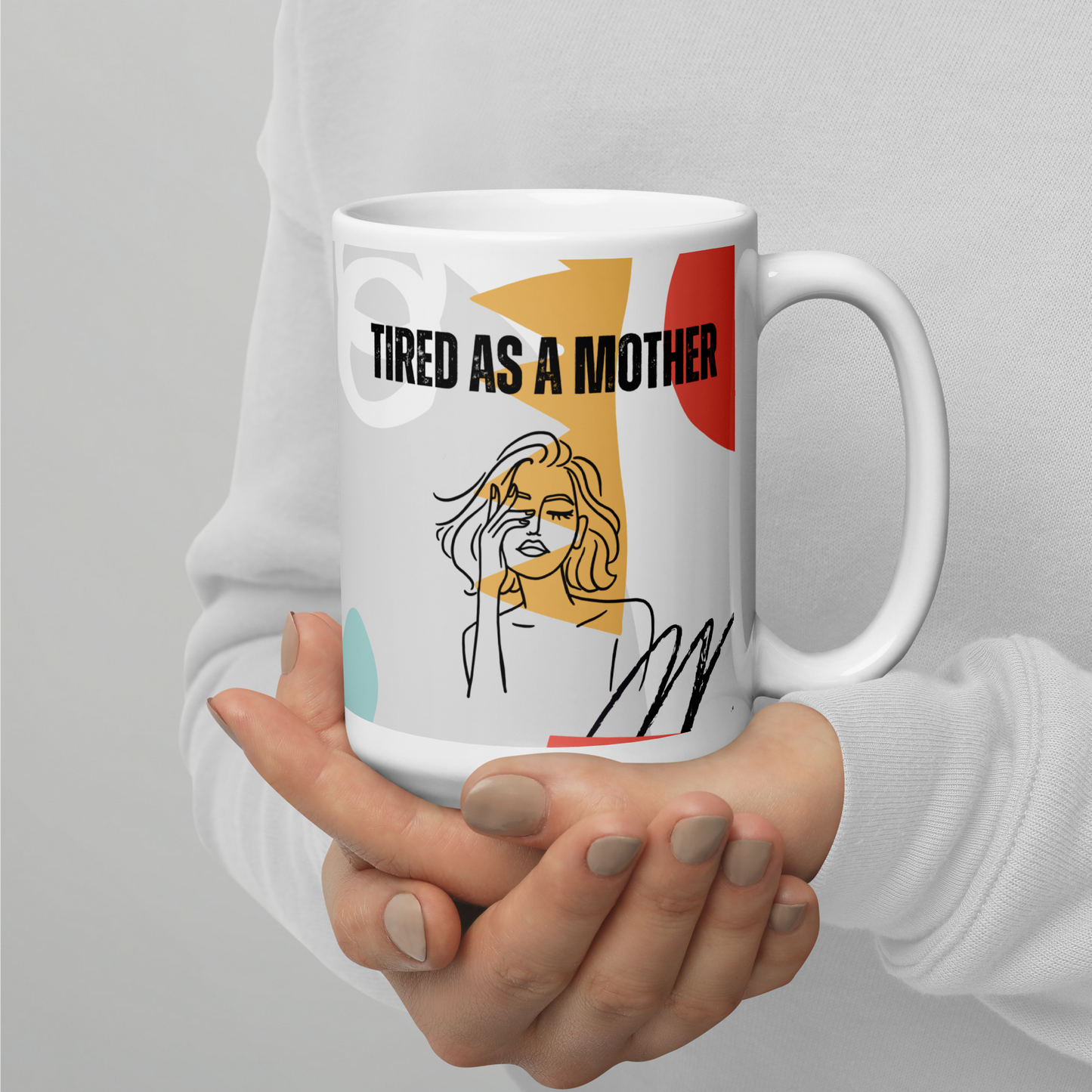 Manicured hands belonging to a person wearing a white sweatshirt cup a colorful coffee mug that reads "TIRED AS A MOTHER". Under the text is line art of a woman with her eyes closed, rubbing one eye. A colorful background pattern includes mint, rosy pink, yellow, coral and black with shapes reminiscent of the 80s or early 90s.