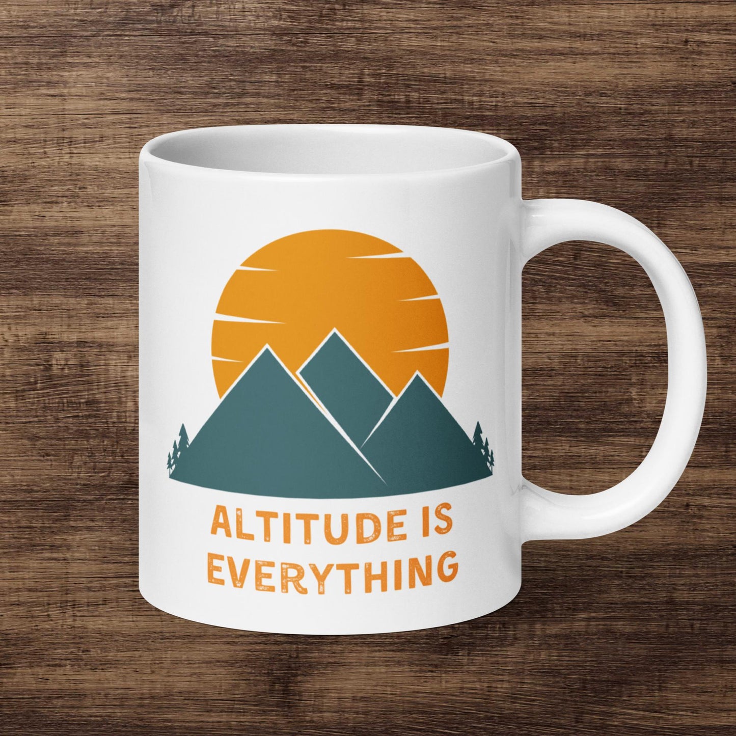 White ceramic mug with an image of mountains and a sunset reads Altitude is Everything. The mug sits in front on an aesthetically pleasing wood panel background.