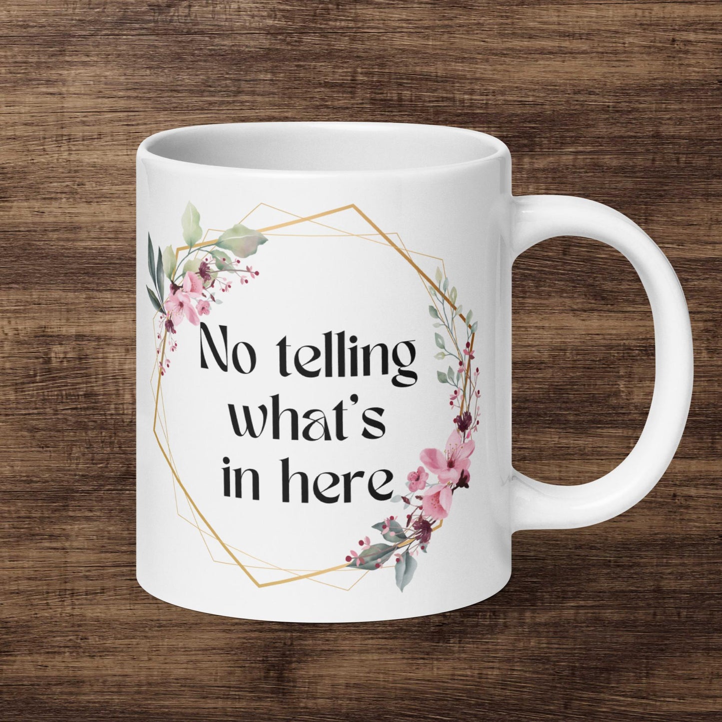 A 20 oz white ceramic mug with the text "NO TELLING WHAT'S IN HERE" sits against a walnut wood backdrop. The mug has a feminine boho feel with a floral and golden border surrounding the text.