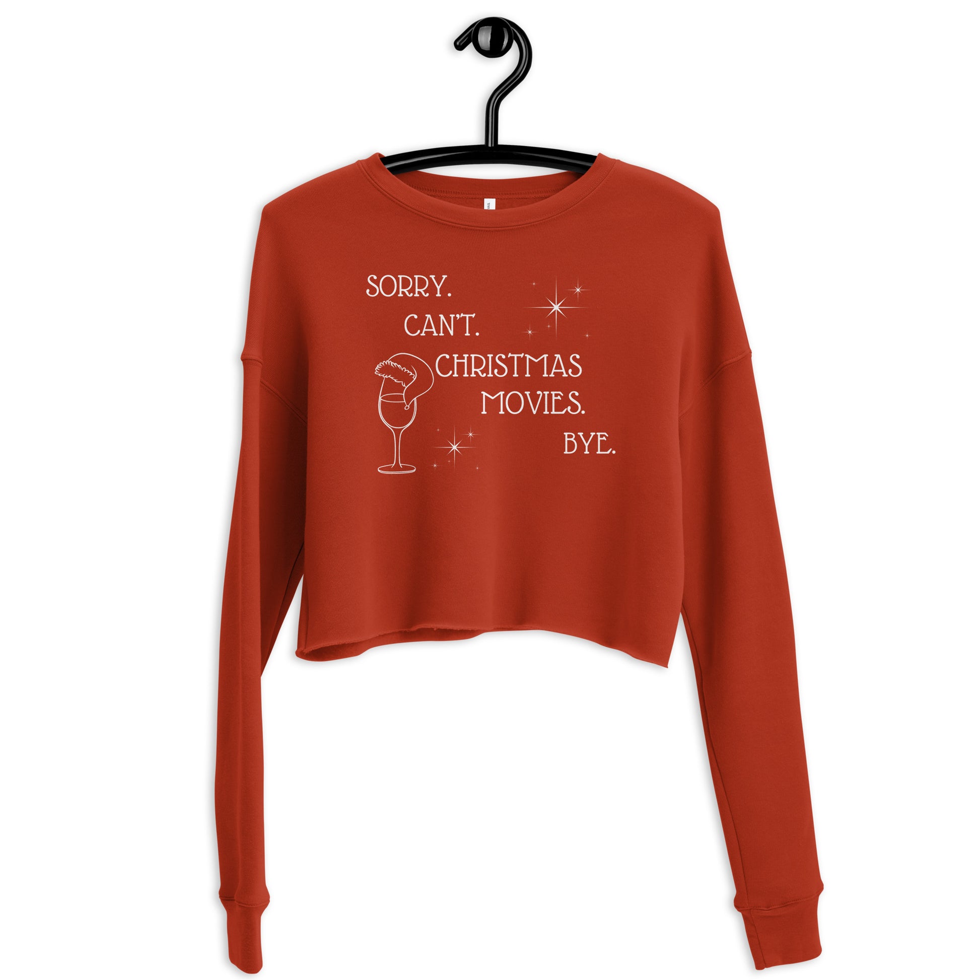 Festive red cropped sweatshirt reads "Sorry. Can't. Christmas Movies. Bye." It's accompanied by a wine glass topped with a Santa hat and star details.