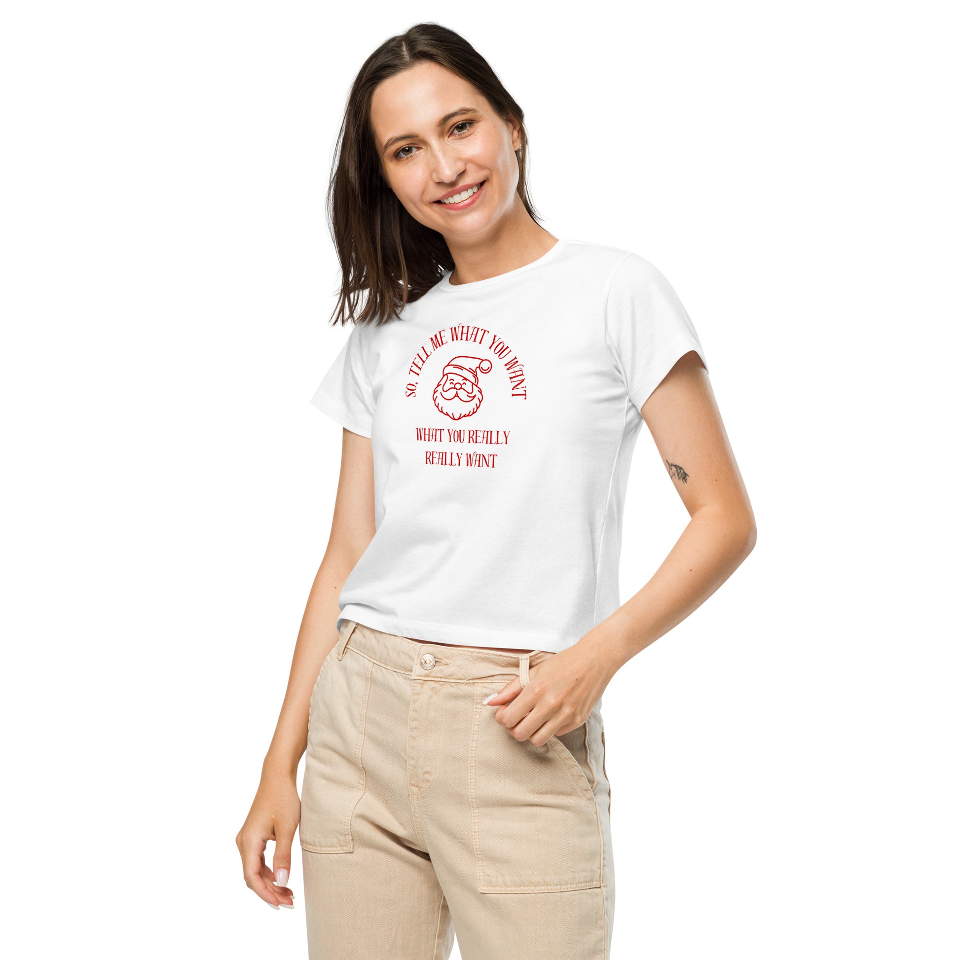 A woman models a fitted white mid-length t-shirt featuring Santa's face and the text "So Tell Me What You Want What You Really Really Want" in red, perfectly hitting at the waistline of her light-colored pants.