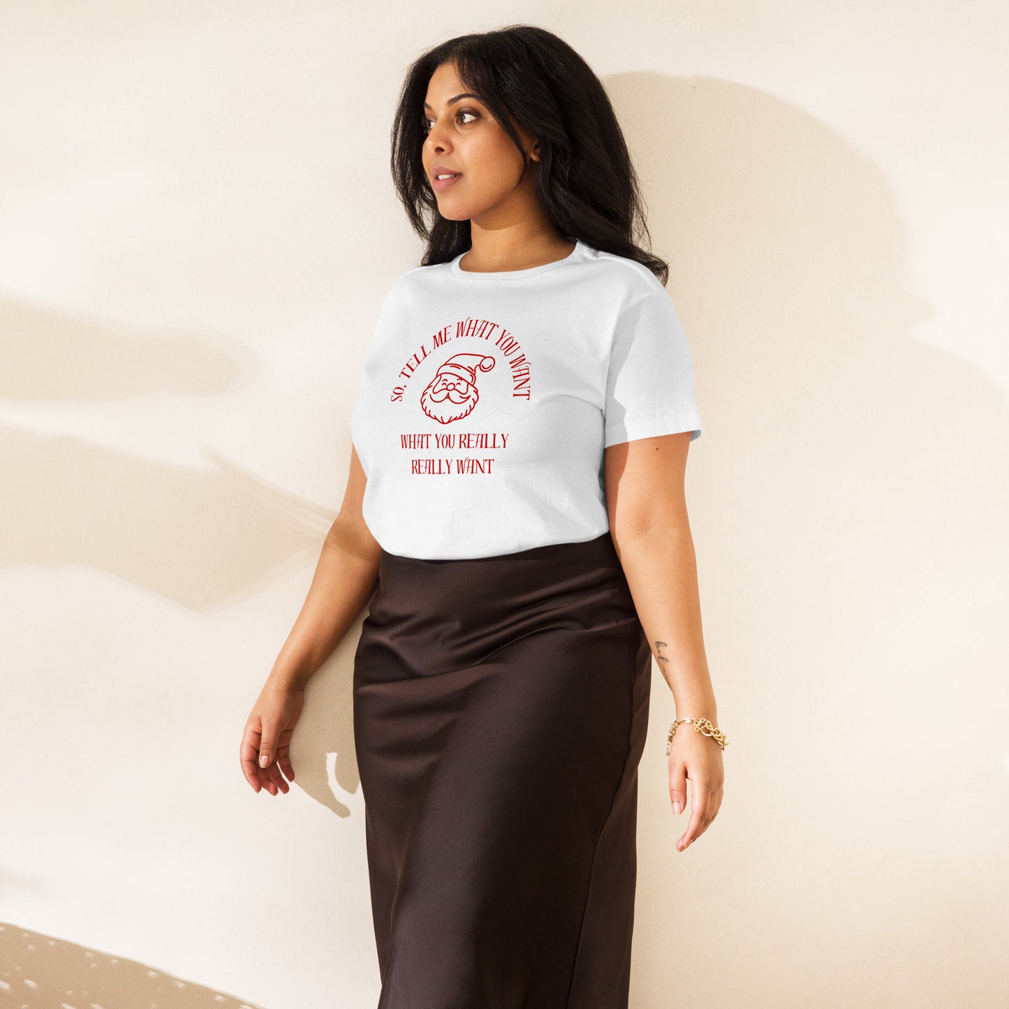 A woman models a fitted white mid-length t-shirt featuring Santa's face and the text "So Tell Me What You Want What You Really Really Want" in red, perfectly tucked into her high waisted skirt.