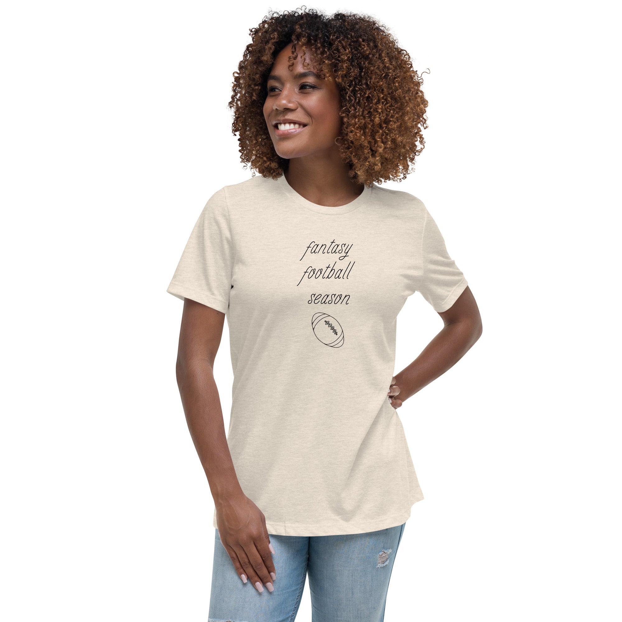 Woman in jeans sports an off-white women's tee shirt that reads "FANTASY FOOTBALL SEASON" along with an image of a football. The font is a thin and flowy cursive that is pretty and feminine.